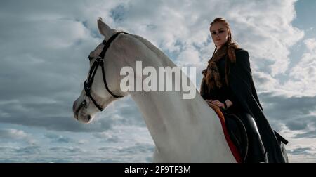 Junge wikingerfrau mit roten Haaren reitet auf einem Pferd. Dramatisches Licht. Rollenspiel Stockfoto