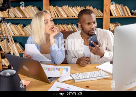 Seriöse Mitarbeiter verwenden verschiedene Gadgets, arbeiten an Finanzberichten, zeichnen Sprachnachrichten an Kollegen auf. Stilvolle Geschäftspartner diskutieren über Neues Stockfoto