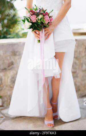 Braut in einem stilvollen Kleid mit offenen Beinen und einem Brautstrauß mit Rosen, veronica, Viburnum und Buchsbaum in den Händen, aus nächster Nähe Stockfoto