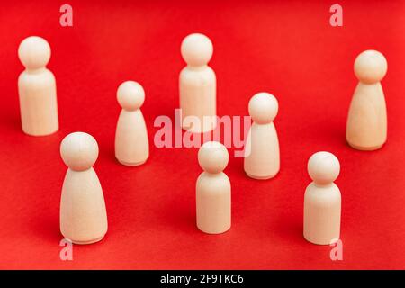 Hölzerne Menschenfiguren stehen vor rotem Hintergrund. Gesellschaftsverhalten, soziale Distanzierung während einer Pandemie. Metapher für Unternehmen, Teamarbeit, Teamvielfalt. Stockfoto