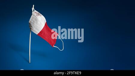 Malta Maske auf dunkelblauem Hintergrund. Winkende Flagge von Malta auf medizinischer Maske auf Stange gemalt. Virenangriff-Flag. Konzept des Banners des Kampfes gegen die Gefechten Stockfoto