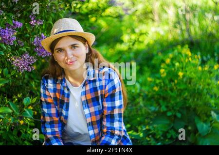 Unschärfe junge Sommerfrau. Schöne Frau im karierten Hemd und Hut mit lila Haufen und Blumenwiese im Frühlingsgarten, Porträt von jungen Stockfoto