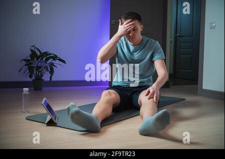 Nach einem harten Heimtraining mit Hilfe des Internets und eines Tablets ist der Sportler in Sportuniform müde. Stockfoto