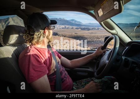 Ein junger Mann blickt aus seinem Fenster auf die Aussicht, während er durch den Death Valley National Park fährt. Stockfoto