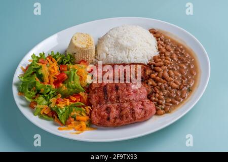 Teller mit Wurst, Bohnen, Reis, Salat und Farofa auf isoliertem neutralem Hintergrund. Mittagessen mit traditioneller brasilianischer Küche. Stockfoto