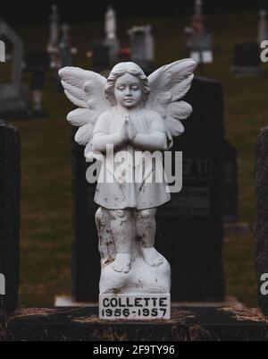 Junge weibliche Engelsstatue, die betet, befindet sich auf einem kleinen Kirchfriedhof Stockfoto