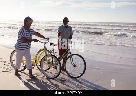 Glückliches älteres afroamerikanisches Paar mit Fahrrädern, die zusammen auf dem Weg sind Der Strand Stockfoto