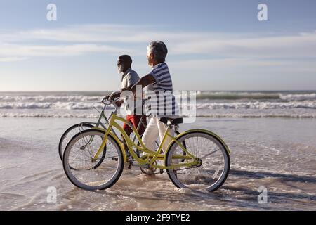 Glückliches älteres afroamerikanisches Paar mit Fahrrädern, die zusammen auf dem Weg sind Der Strand Stockfoto