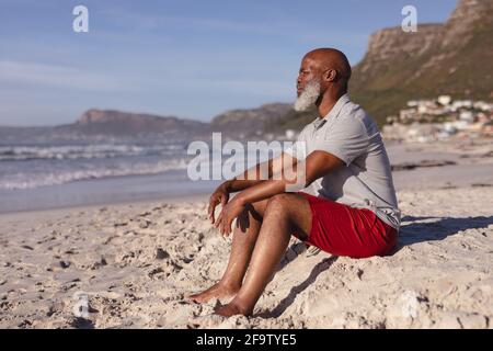Nachdenklicher älterer afroamerikanischer Mann, der alleine am Strand sitzt Stockfoto