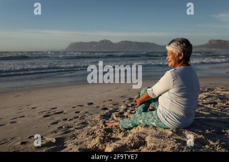 Ältere afroamerikanische Frau, die lächelt, während sie am Strand sitzt Stockfoto