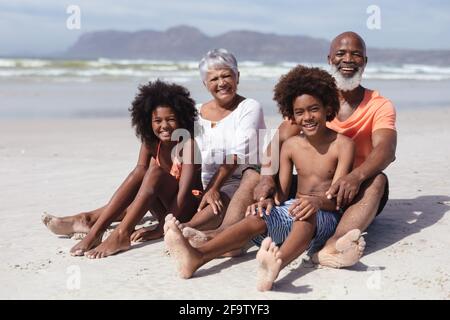 Porträt afroamerikanischer Großeltern und Enkelkinder, die lächeln, während sie sitzen Am Strand Stockfoto