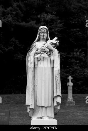 Statue in einem Kirchfriedhof von Maria, die ein Kreuz hält Über ihre Schulter Stockfoto