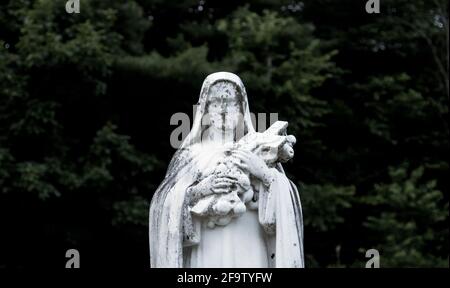 Statue der Jungfrau Maria draußen auf einem Kirchfriedhof Mit einem dunkelgrünen Hintergrund Stockfoto