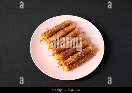 Hausgemachte Churro Bites auf einem rosa Teller auf schwarzem Hintergrund, Seitenansicht. Stockfoto