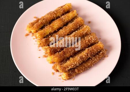 Selbst gebackene Churro Bites auf einem rosa Teller auf einem schwarzen Hintergrund, Blick aus dem unteren Winkel. Stockfoto