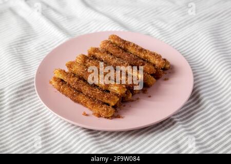 Selbstgebackene Churro Bites auf einem rosa Teller auf Stoff, Seitenansicht. Stockfoto