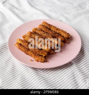 Selbst gebackene Churro Bites auf einem rosa Teller auf Stoff, Blick aus der Ferne. Stockfoto