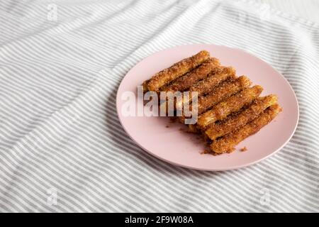 Selbstgebackene Churro Bites auf einem rosa Teller auf Stoff, Seitenansicht. Speicherplatz kopieren. Stockfoto