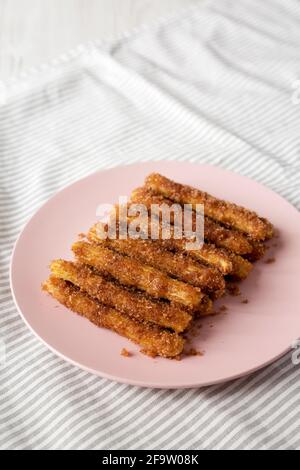 Selbst gebackene Churro Bites auf einem rosa Teller auf Stoff, Blick aus der Ferne. Speicherplatz kopieren. Stockfoto