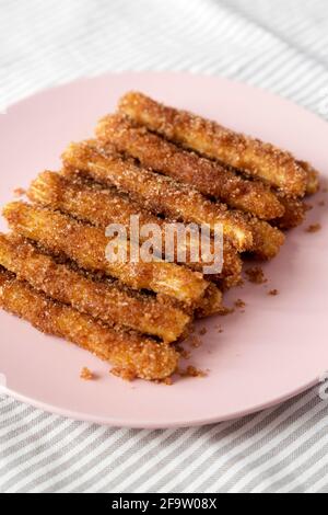 Selbstgebackene Churro Bites auf einem rosa Teller auf Stoff, Seitenansicht. Nahaufnahme. Stockfoto