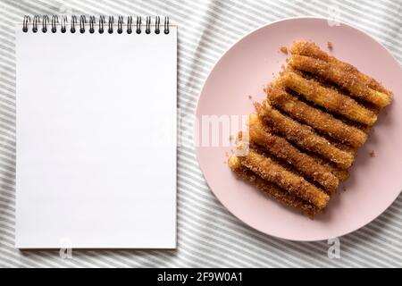 Hausgemachte Churro Bites auf einem rosa Teller, leerer Notizblock, Draufsicht. Flach liegend, über Kopf, von oben. Stockfoto