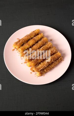 Hausgemachte Churro Bites auf einem rosa Teller auf einer schwarzen Oberfläche, Seitenansicht. Stockfoto