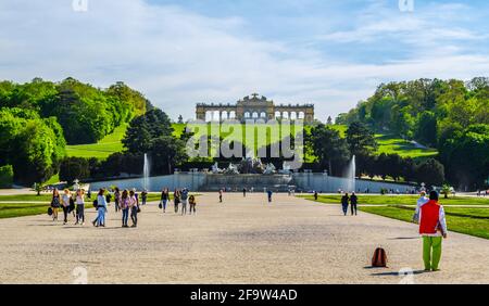 WIEN, ÖSTERREICH, 30. APRIL 2015: Blick auf das grüne Blumenbeet, Menschen gehen in Richtung Neptunbrunnen und Gloriette am Schönbrunn, Wien, Österreich Stockfoto