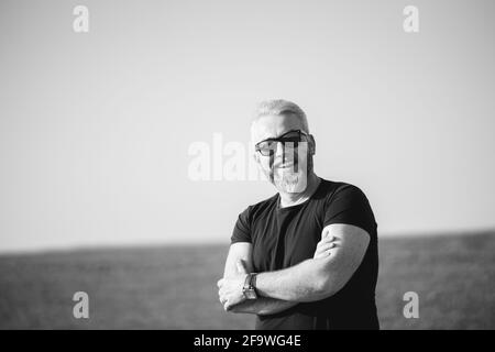 Graustufen-Aufnahme eines fröhlichen Mannes mit grauem Haar, das lächelt Auf dem Hintergrund eines Feldes Stockfoto