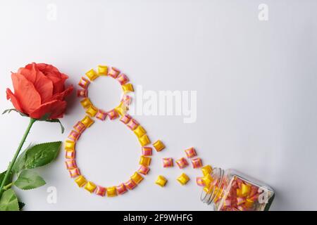 Eine rote Rose auf weißem Hintergrund mit hellen Süßigkeiten Aus dem Glas in der Form Stockfoto