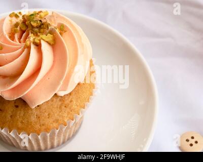 Hübscher Cupcake mit pinker Glasur auf einer leuchtend weißen Struktur Hintergrund Stockfoto