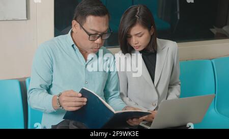 Junge asiatische Geschäftsfrau und Mann sitzen mit Laptop-Computer Arbeiten Gespräch erklären zusammen auf der U-Bahn-Zug in der Morgens während der Reise nach w Stockfoto