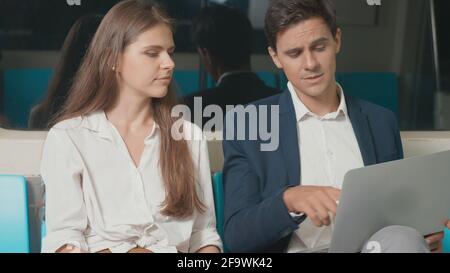 Junge kaukasische weiße Geschäftsfrau und Mann, die mit einem Laptop sitzen Computer arbeitet zusammen im Gespräch auf der U-Bahn-Zug in der Morgen während des Ausgehend zu Stockfoto