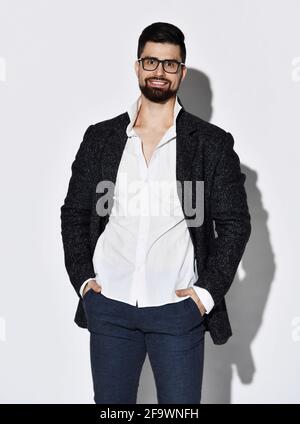 Freundlich lächelnder stilvoller bärtiger Mann in Brille, lässige Tweed-Jacke und Jeans stehen mit Händen in den Taschen Stockfoto