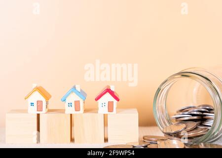 Haus auf Holzblock und Münze im Glas isoliert orange Hintergrund. Geld sparen und Investitionskonzept. Stockfoto