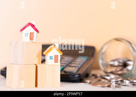 Haus auf Holzblock und Münze im Glas und Rechner isoliert orange Hintergrund. Geld sparen und Investitionskonzept. Stockfoto