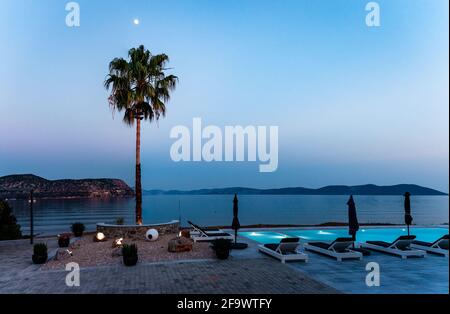 Ein Pool am Meer in der Nacht. Mond über einer Palme. Foto aufgenommen in Ermioni, Peloponnes, Griechenland. Stockfoto