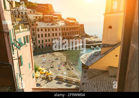 Vernazza, Ligurien, Italien. Juni 2020. Eine Sicht zwischen den Häusern mit Blick auf den Strand des Dorfes. Die Menschen baden im Wasser des Yachthafens Stockfoto