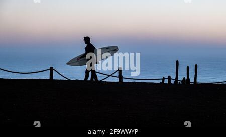 Surfer zu Fuß zum Meer, Silhouette des Menschen bei einem Sonnenaufgang in punta de lobos pichilemu chile. Stockfoto