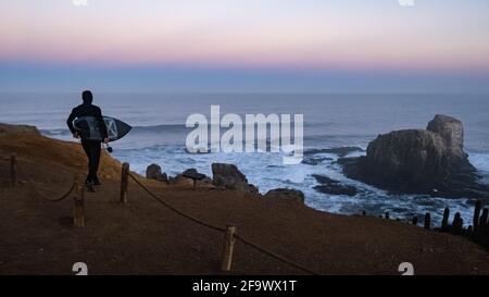 Surfer gehen surfen, blaue Stunde, schwarzes Surfbrett und Neoprenanzug, Sonnenaufgang in punta de lobos Pichilemu Chile Stockfoto