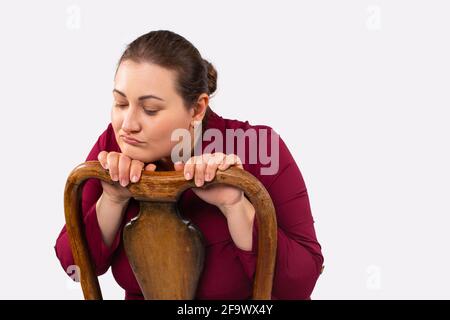 Traurige, nachdenkliche und große Frau, die auf einem Stuhl sitzt und sich deprimiert, beleidigt, einsam, verärgert, plump fühlt Stockfoto