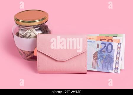 Amerikanische Dollar in Glas-Geldglas mit leerem Etikett und rosa Brieftasche voller Euro-Banknoten, finanzielle, Sparen, Austausch, Diversifizierung. JAR voll mit Stockfoto