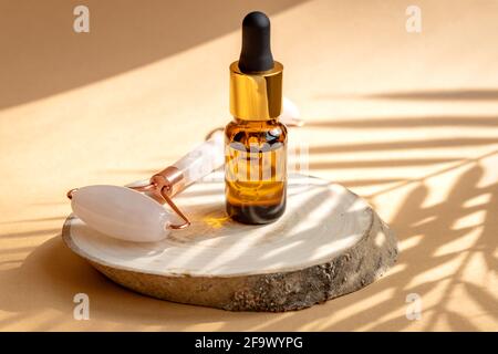 Komposition mit natürlicher SPA-Kosmetik und Geräten für die Gesichtspflege. Tropfflasche aus dunklem Glas mit ätherischen Ölen aus biologischem Anbau und Gesichtsmassageroller Stockfoto