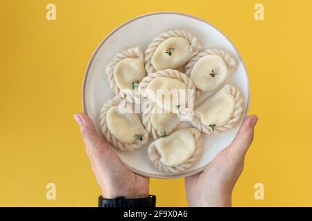 Weibliche Hände servieren köstliche, frische, hausgemachte italienische Ravioli auf einem Tonteller auf gelbem Hintergrund. Stockfoto