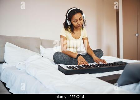 Schöne junge Frau in Kopfhörern spielen Synthesizer zu Hause Stockfoto