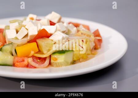 Griechischer Salat auf weißem Teller auf grauem Hintergrund. Stockfoto