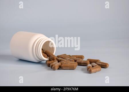 Natürliche braune Kapseln mit gepressten Heilkräutern, Pillen in offenem umgedrehtem Plastikglas auf der Vorderseite des Tisches. Alternative Medizin Konzept der Medikamente, Tabletten Stockfoto