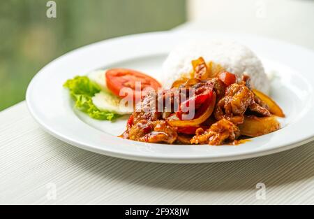 Gebratenes Schweinefleisch mit traditioneller thailändischer Chili-Paste oder Moo Pad Prickpow in Thailändischer Sprache mit weißem Jasminreis, natürliches Licht aus dem Fenster. Stockfoto