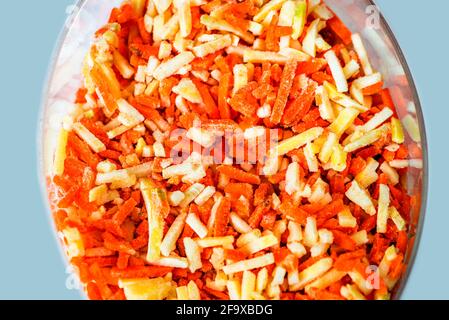 Haufen gefrorenes Gemüse (Karotte, Petersilie und Sellerie) in dünne kleine Stücke (Julienne) in Glasschüssel geschnitten, Draufsicht. Stockfoto