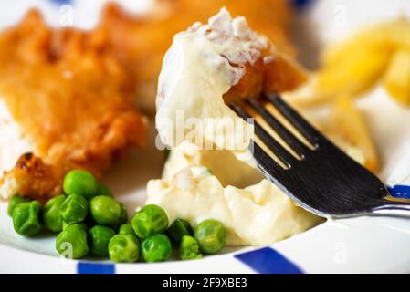 Teller mit traditionellem Streetfood-Gericht, panierter gebratener Fisch und Pommes mit Erbse und Mayonnaise, Stück Fisch mit Mayonnaise auf der Gabel, Nahaufnahme. Stockfoto