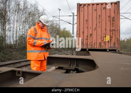 Ein Eisenbahner, der in einem vollständigen Rohr inspiziert und einen inspiziert Versand Container Güterzug in Großbritannien Stockfoto